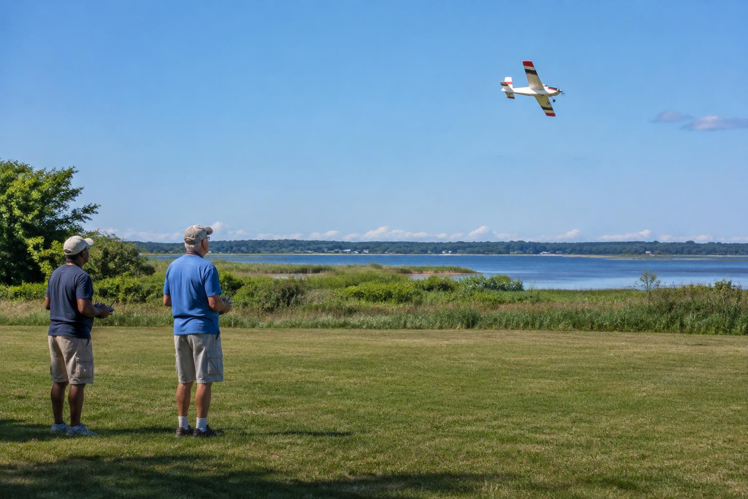 Club members flying a radio-controlled airplane at a waterfront field